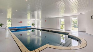 Ein großer, überdachter Pool mit blauer Liegefläche, großen Fenstern und einer weißen Decke.