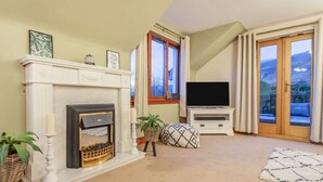 Ein Wohnzimmer mit Kamin, Fernseher und Blick ins Freie.
