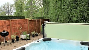 Ein Whirlpool in einem Garten mit Holzzaun, Blumentöpfen und einem Grill.