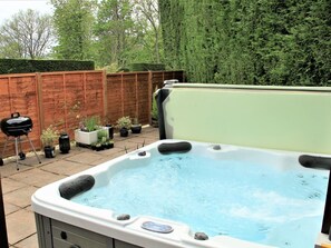 A hot tub in a backyard with a wooden fence, potted plants, and a barbecue grill.