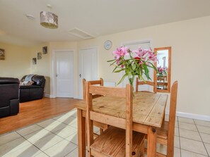 A dining area with a wooden table and chairs, a vase of flowers, and a black leather sofa.