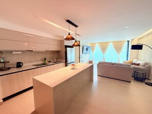 A modern kitchen with a central island, a dining area with a sofa, and a living room with a TV. - Oceanfront Condo (Mazatlán)