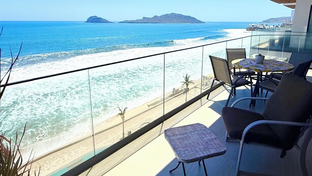 Een balkon met glazen hekwerk met uitzicht op een strand en oceaan.