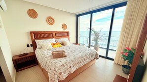 Een slaapkamer met een groot bed, een nachtkastje, een kamerplant en uitzicht op zee.