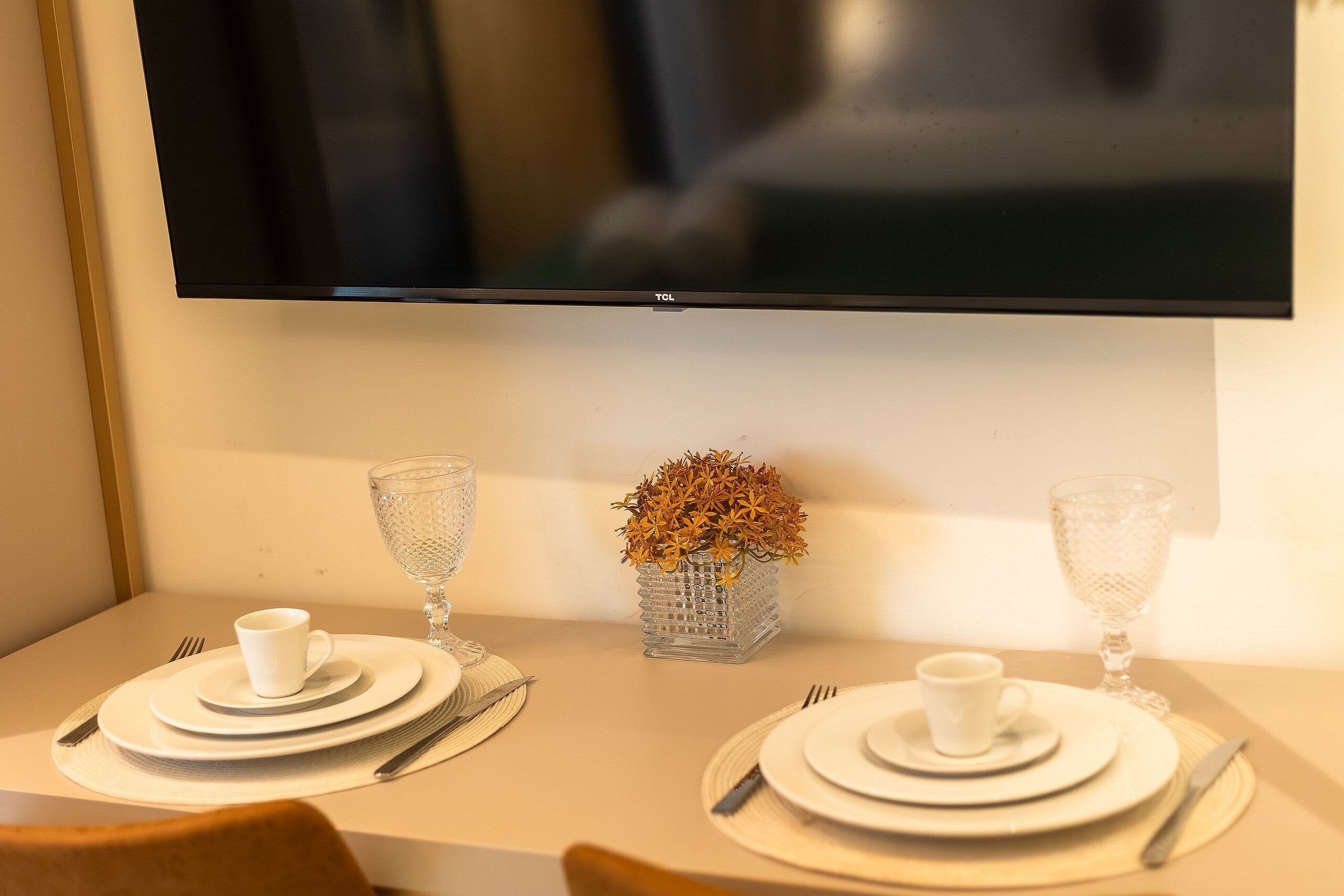 A dining table set with plates, cutlery, and a vase with dried flowers.