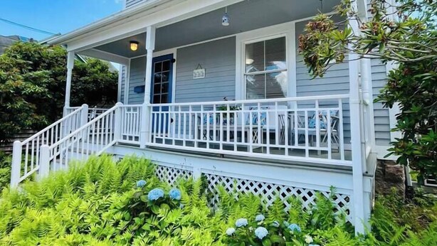 Ein zweistöckiges Haus mit Veranda, überdachtem Eingangsbereich und einem gepflegten Garten mit verschiedenen Pflanzen und Blumen.
