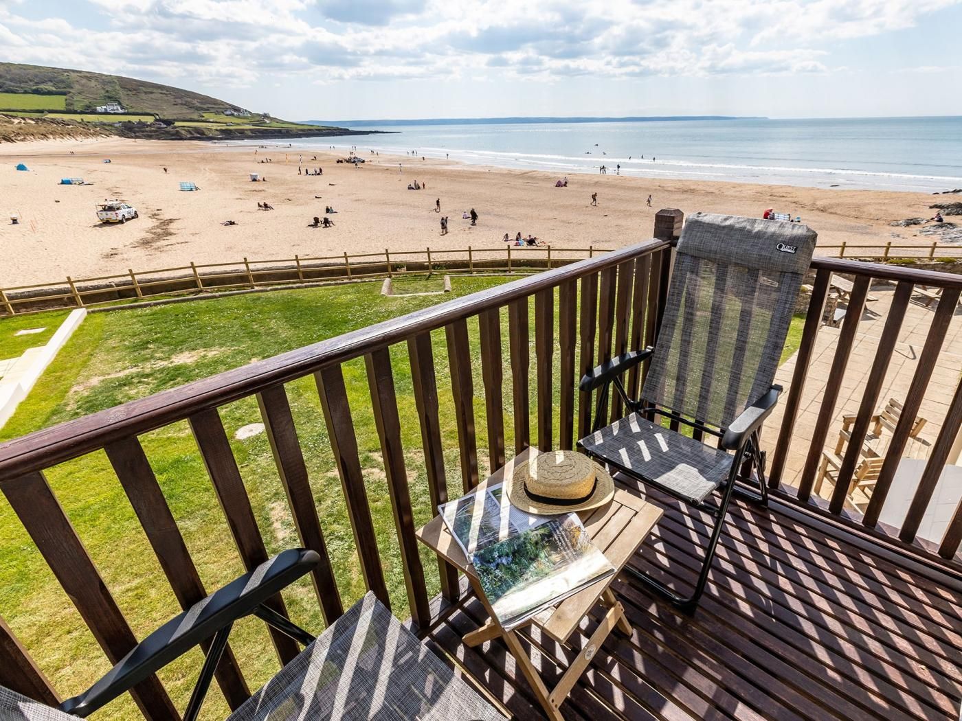 A balcony with a view of a beach, a table with a magazine, and a hat.