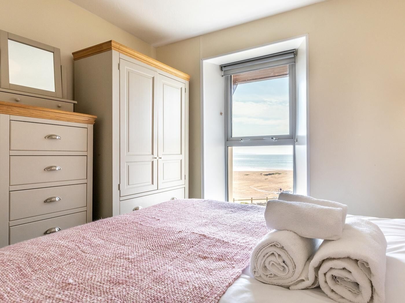 Un dormitorio con cama, cómoda, ventana con vista a la playa y persiana.