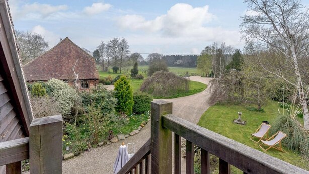 A wooden deck with a view of a rural landscape, including a thatched-roof building and a grassy area with two lounge chairs. - 1 Bed in Cranbrook (oc-87119) (Benenden)