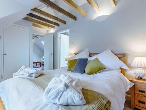 Een slaapkamer met een bed, kussens, een nachtkastje met een lamp en een houten plafond.