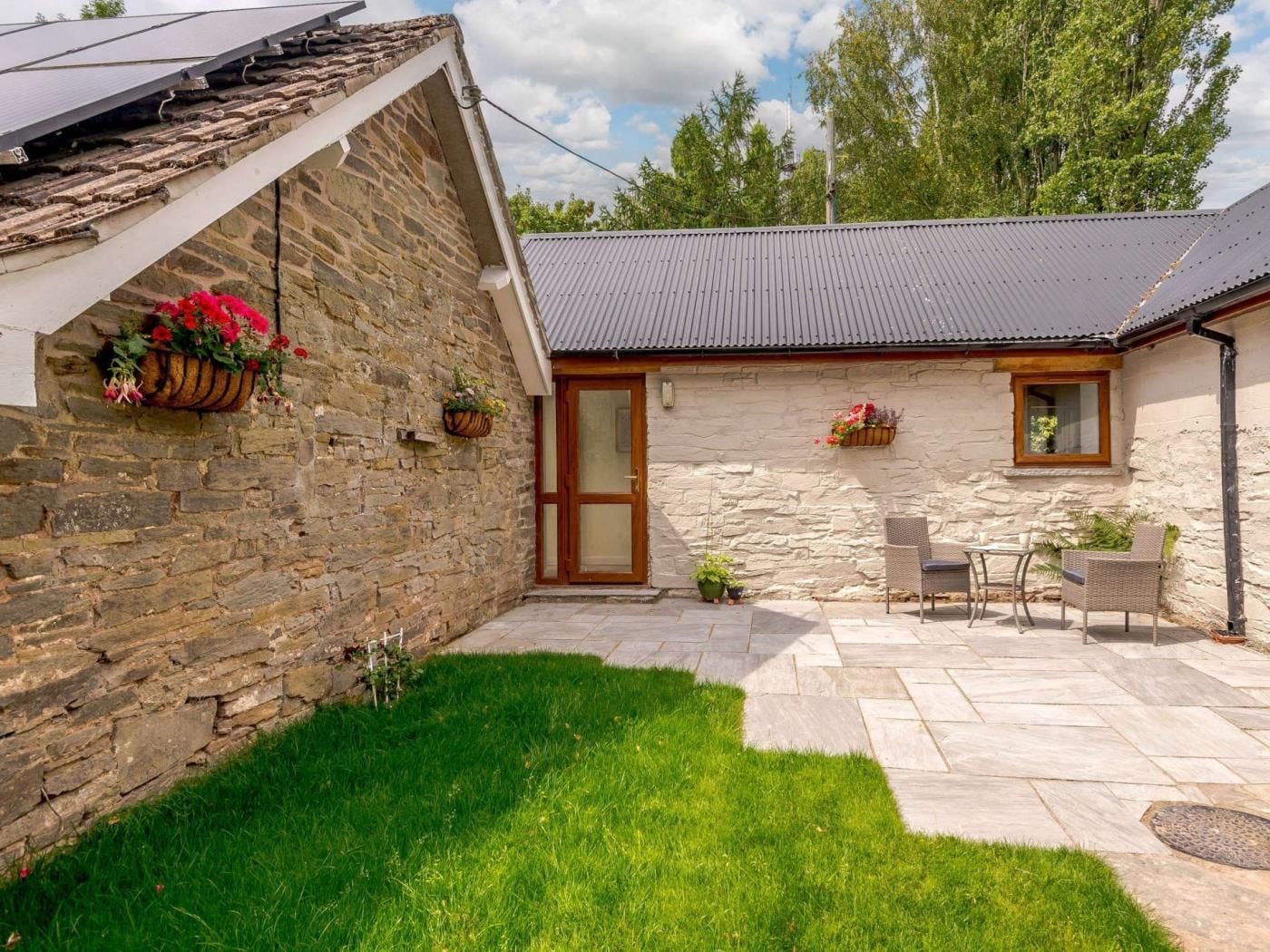 A stone building with a tiled roof, a grassy yard, and outdoor seating.