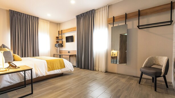 Ett hotellrum med en säng, ett skrivbord, en stol, en tv och en spegel.