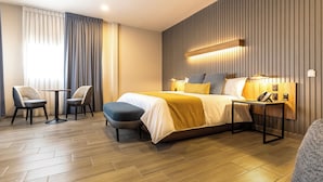 A modern hotel room with a bed, bedside tables, a chair, and a desk.