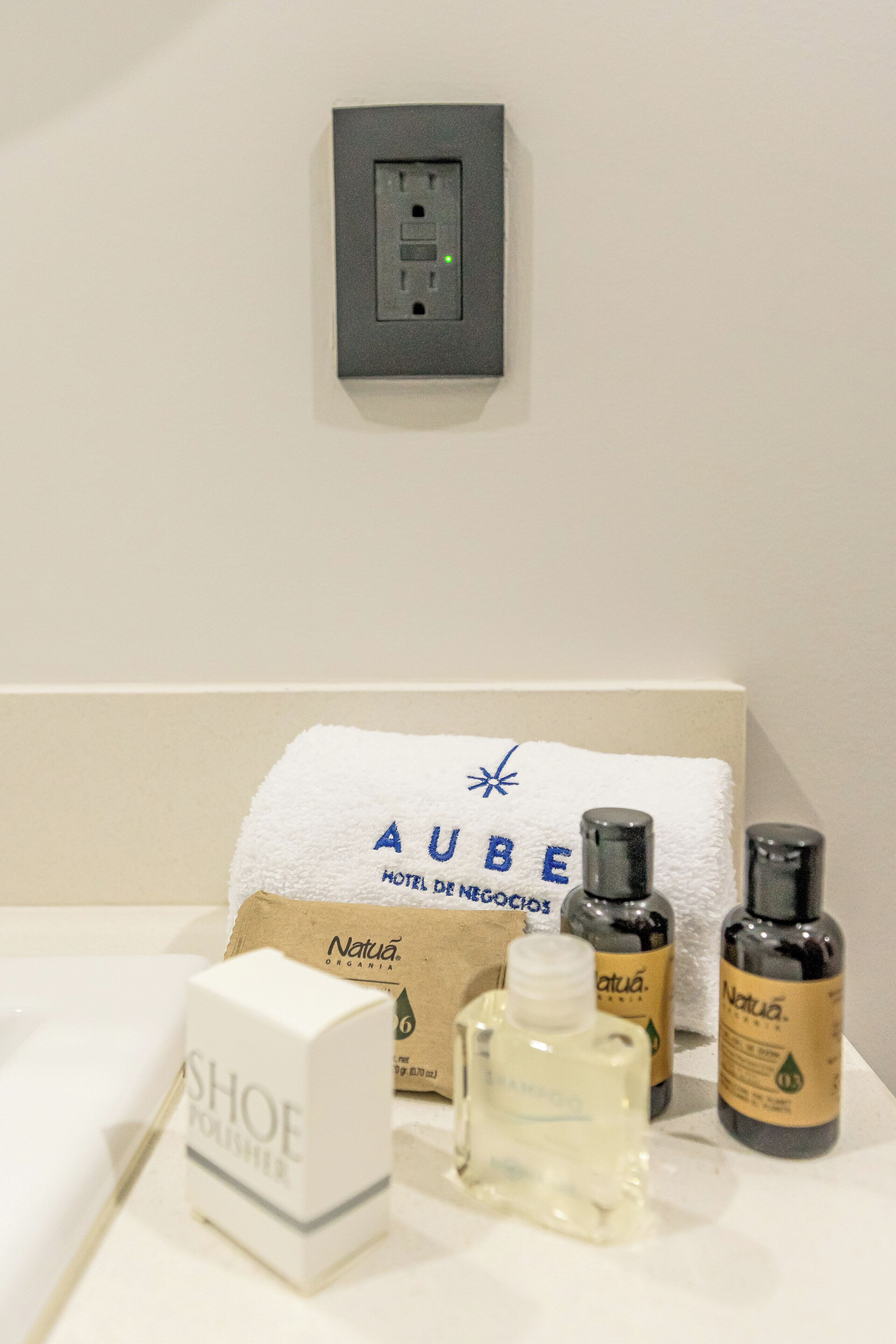 Een hotelbadkamer met een handdoek, een fles Natuá Organía, een fles Natuá, en een doos SHOE.