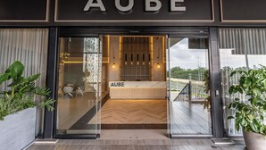 A hotel entrance with a reception desk labeled 'AUBE' and a view of the interior.