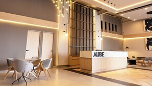 Ett modernt receptionsområde med en receptionsdisk märkt med texten ”AUBE”, samtida möbler och en stilfull hänglampa.