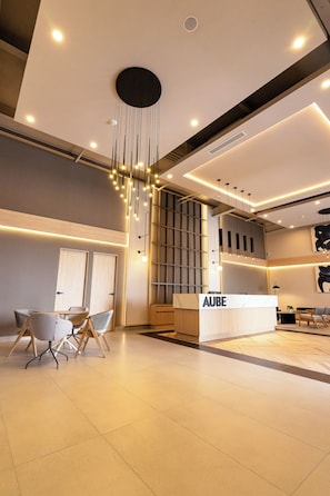 A modern reception area with a reception desk labeled 'AUBE,' contemporary furniture, and a stylish pendant light fixture.