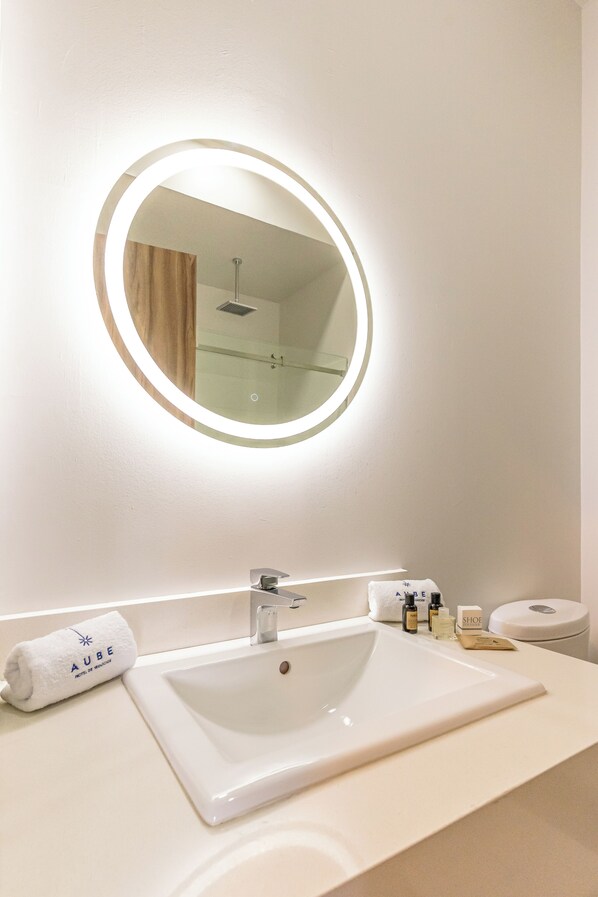 A hotel bathroom with a round mirror, a sink, and toiletries on the counter.