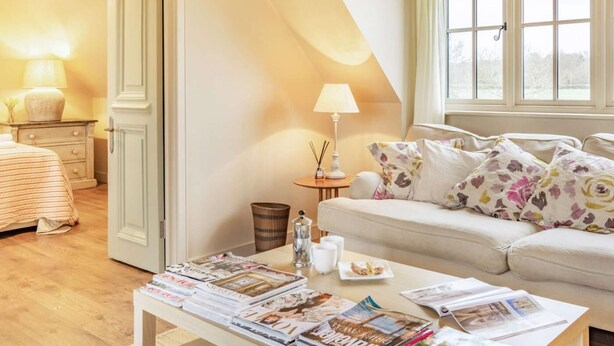 En hyggelig stue med sofa, sofabord med magasiner, lampe og et vindue med gardiner.