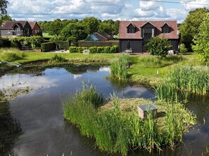 A serene pond with surrounding greenery and a traditional house with a pitched roof. - 1 Bed in Horsham (oc-86961) (Rudgwick)