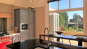A modern kitchen with a central island, a red stove, a microwave, and a chandelier. - 5 Bed in Sandown (oc-87008) (Sandown)