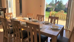 A dining area with a table set for six, large windows, and a view of a garden. - 5 Bed in Sandown (oc-87008) (Sandown)