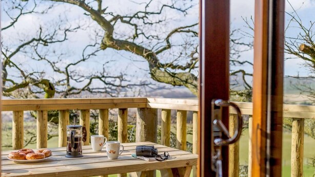 En træterrasse med et bord dækket til morgenmad, blandt andet wienerbrød, en kaffekande og kopper.