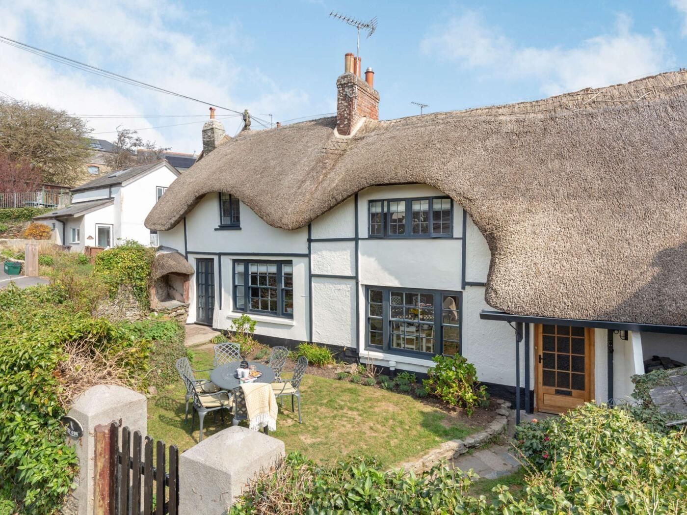 A thatched-roof cottage with a garden and a small table with chairs.