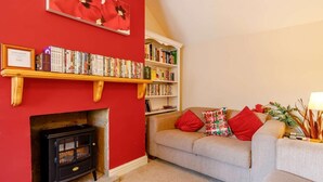 Ein gemütliches Wohnzimmer mit Kamin, Bücherregalen, einer Couch und einer roten Wand.