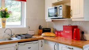 Eine Küche mit weißen Schränken, einer Mikrowelle, einer Brokkiste und einer roten Tasche mit der Aufschrift 'Brot Tee Zucker Kekse'.