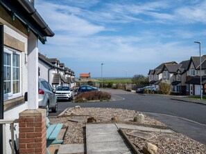 A residential street with houses, parked cars, and a clear view of the sea. - 2 Bed in Seahouses (oc-87389) (Seahouses)