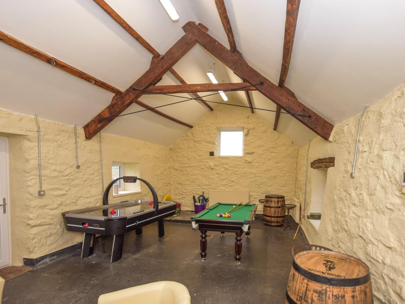 A room with a pool table, a billiards table, a wooden barrel, and a stone wall.