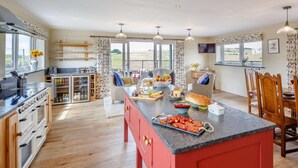Una cocina amplia con una isla central, armarios de madera y un gran ventanal con vistas a un paisaje pintoresco.