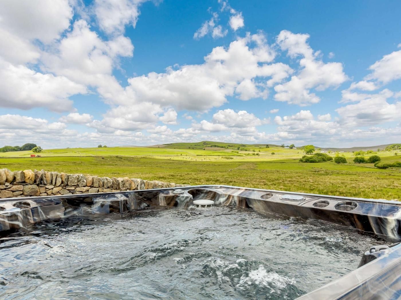 Een bubbelbad met een stenen muur op de voorgrond en een groen landschap op de achtergrond.