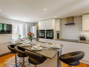 Una cocina moderna con armarios blancos, una isla central con taburetes y vistas al exterior.