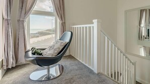Une chambre avec vue sur la plage, une chaise avec un coussin et une rambarde blanche.