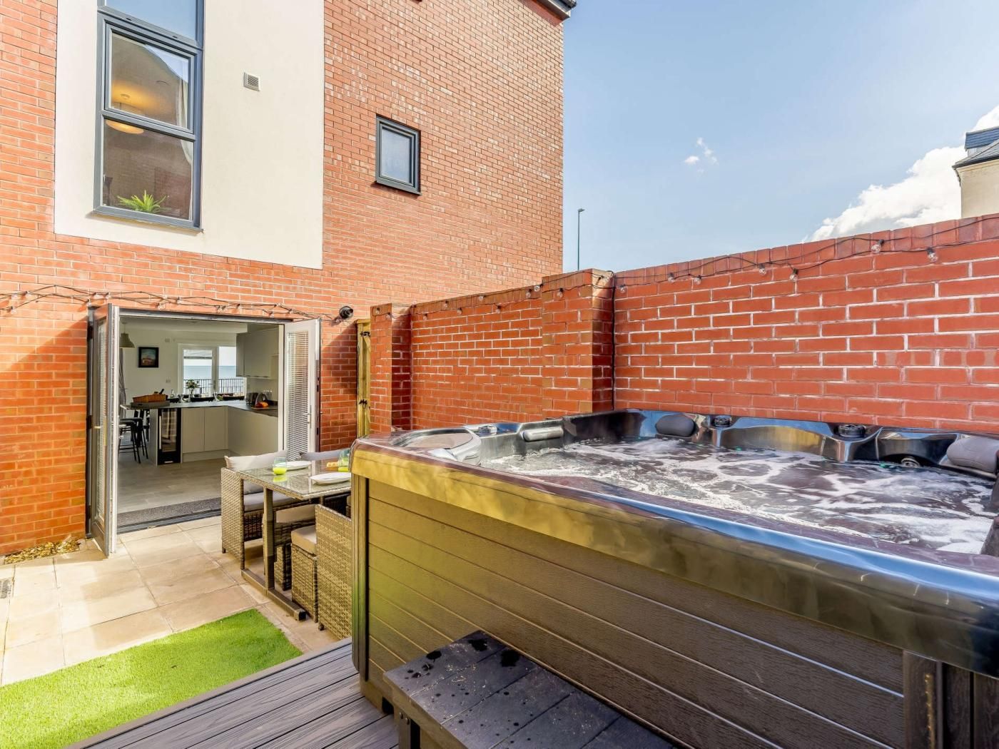 Un patio trasero con un jacuzzi, una terraza de madera y un muro de ladrillo.
