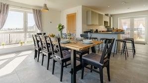 Un espace repas avec une table en bois, des chaises noires et des luminaires suspendus.