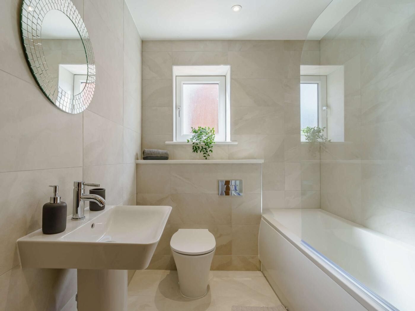 Een moderne badkamer met een wastafel, toilet en bad, een spiegel en een raam met een plant.