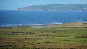 A coastal landscape with a grassy field, a rocky shoreline, and a distant hill. - 4 Bed in Bideford (oc-87428) (Northam)