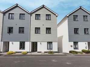 Eine Reihe moderner, zweistöckiger Reihenhäuser mit einheitlicher Fassade und kleinen Vorgärten, bewölkter Himmel.