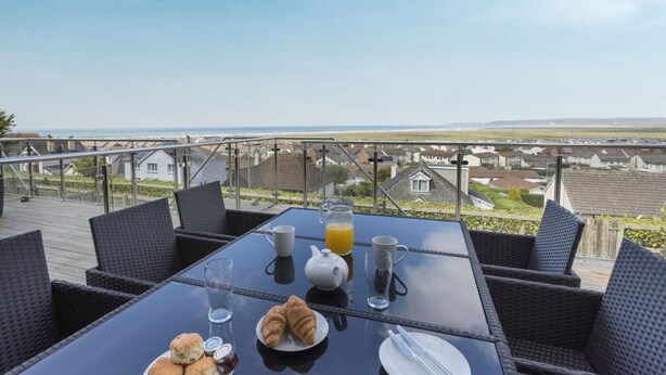 A table set with breakfast items, including croissants, biscuits, and juice, overlooking a coastal view. - 4 Bed in Bideford (oc-87428) (Northam)