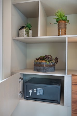 A storage unit with a black safe, a woven basket with plants, and a decorative pot on a shelf. - TO BE SUITES (Ciudad de México)