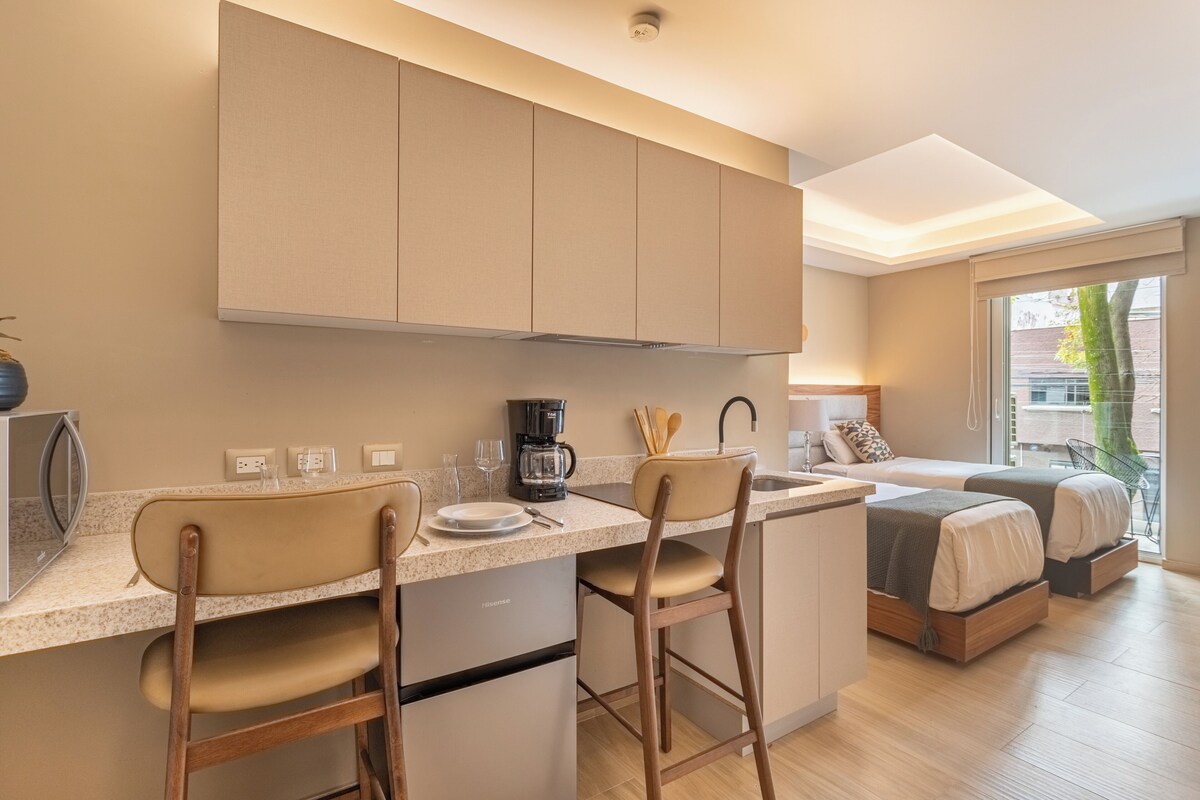 A compact kitchen with a microwave, coffee maker, and bar stools.