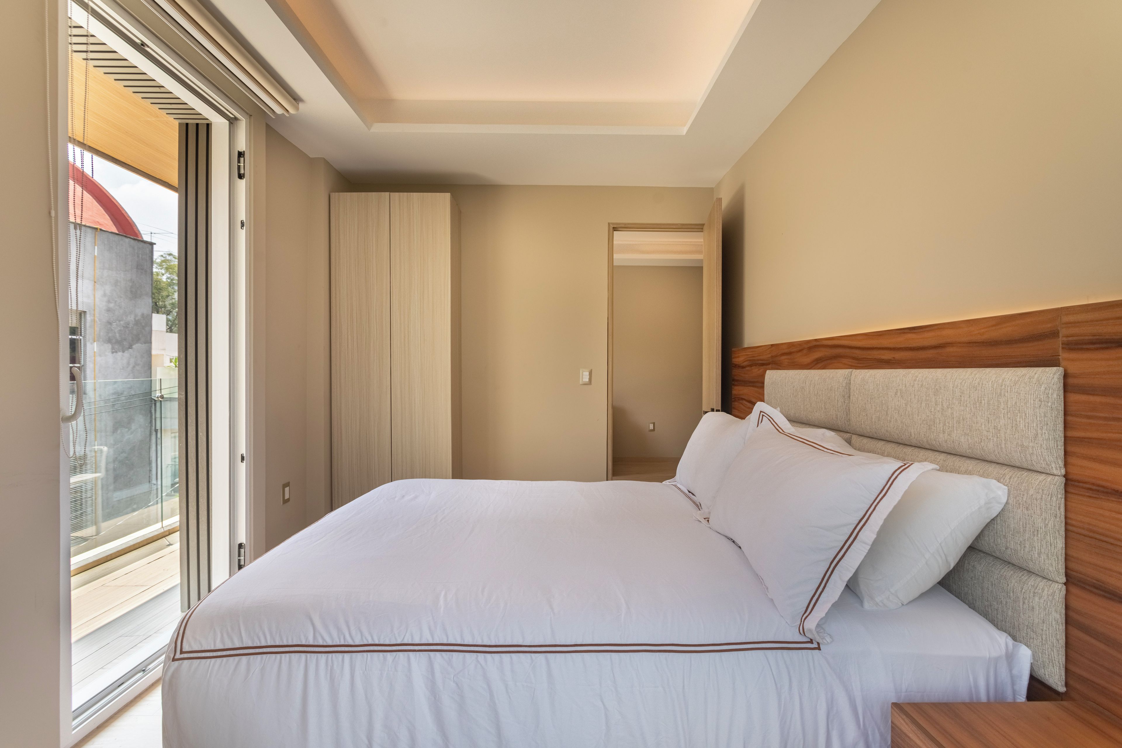 A bedroom with a large bed, a wooden headboard, and a sliding glass door leading to a balcony.