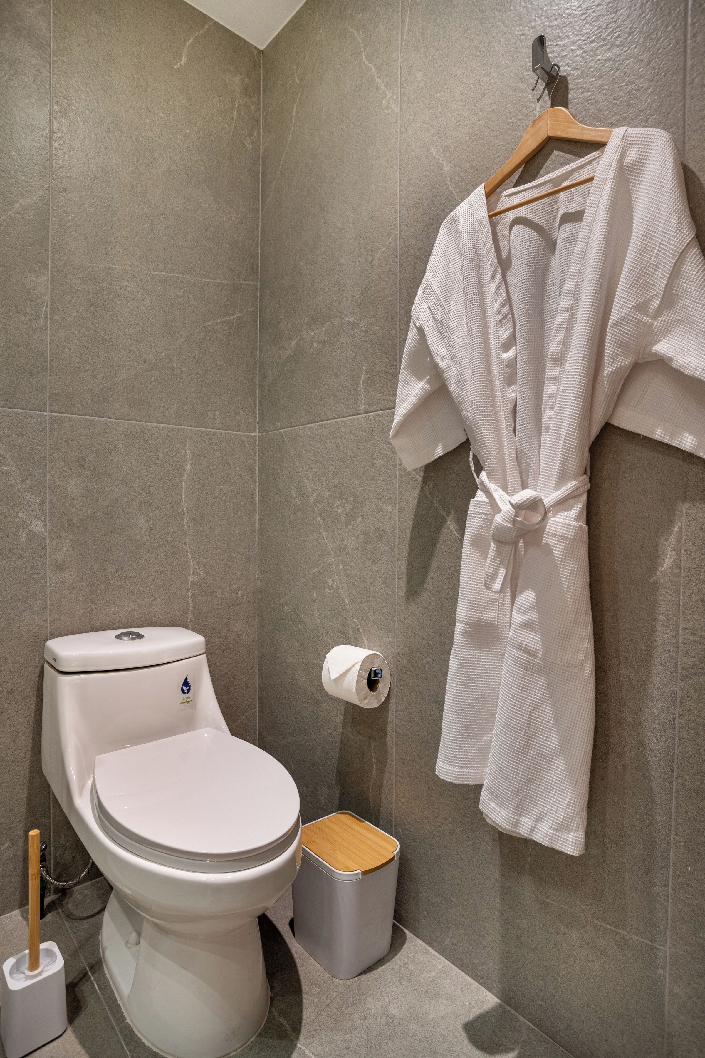 Une salle de bain équipée d’un WC, d’un bidet, d’une poubelle, d’une serviette suspendue et d’un rouleau de papier toilette.
