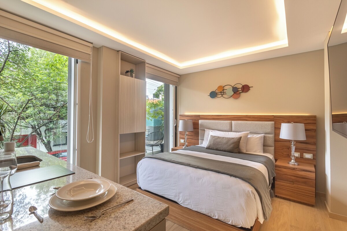 A modern bedroom with a large bed, bedside lamps, a wooden headboard, and a view of greenery outside.