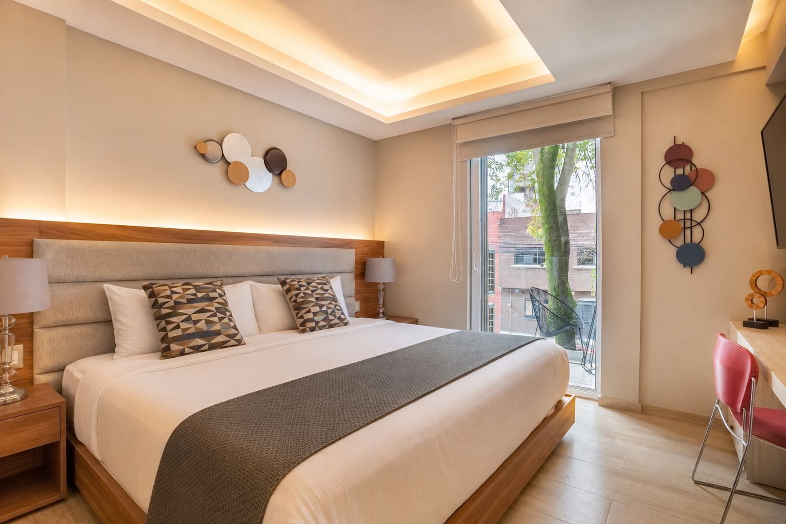 A modern hotel room with a large bed, a wooden headboard, and a view of the outside.