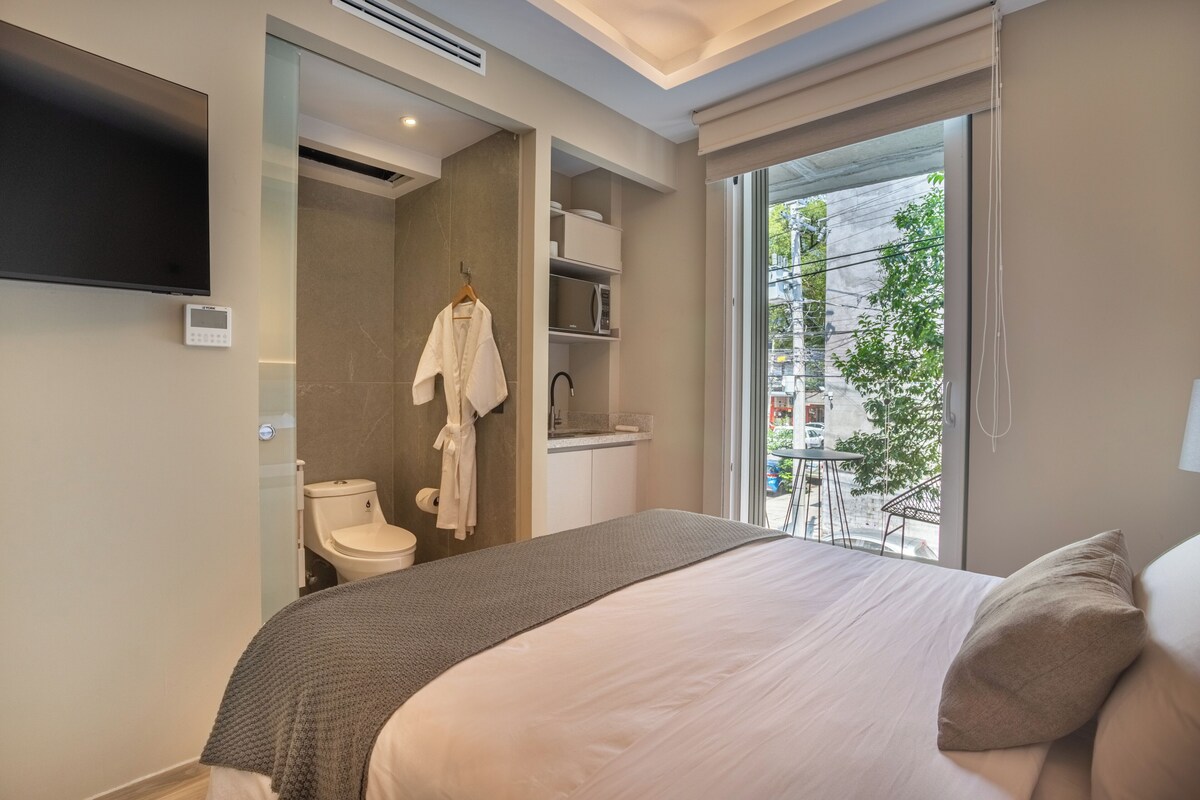 A modern hotel room with a bed, a television, a bathroom, and a view of the city.