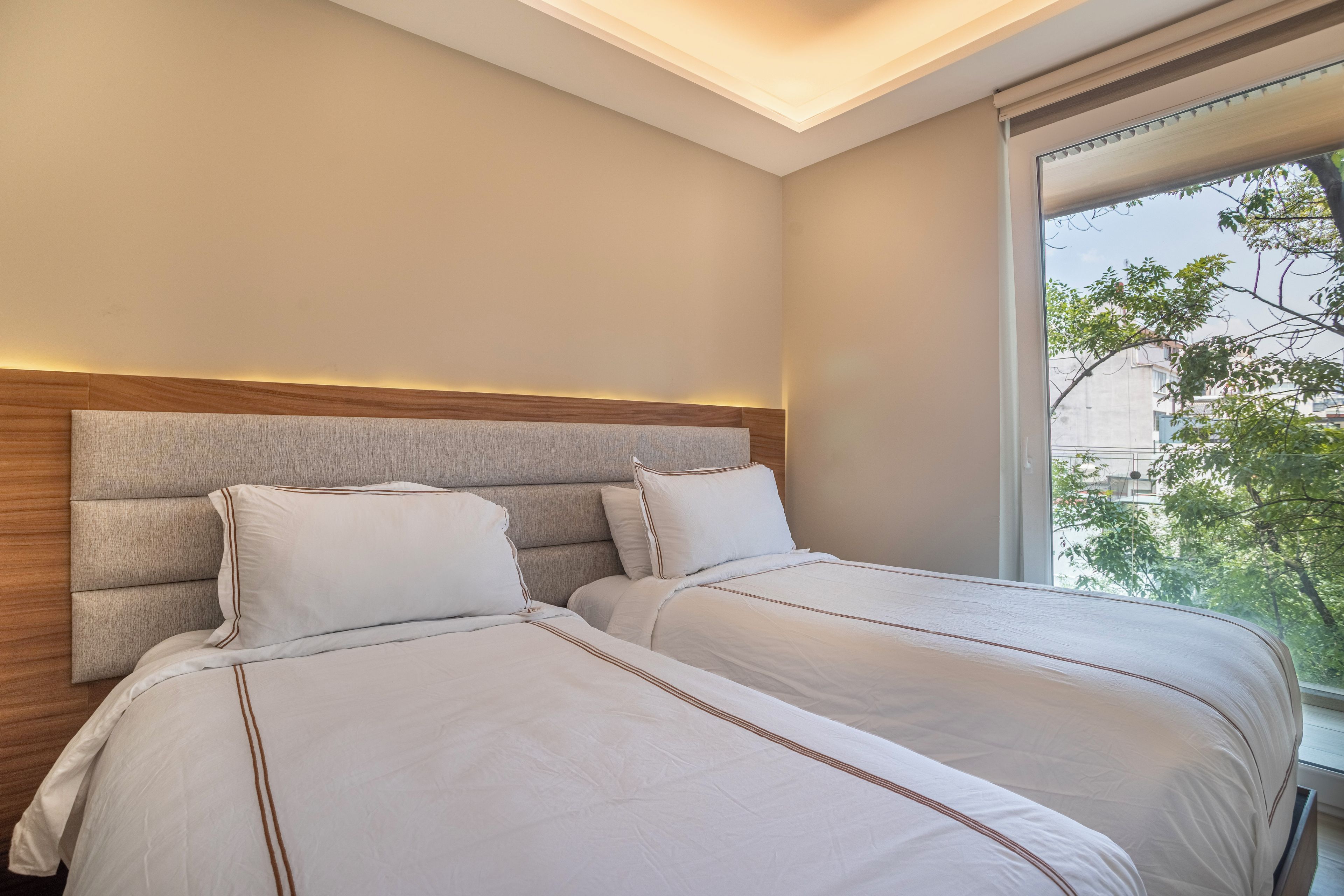 A hotel room with a large window, a wooden headboard, and two beds with white bedding.